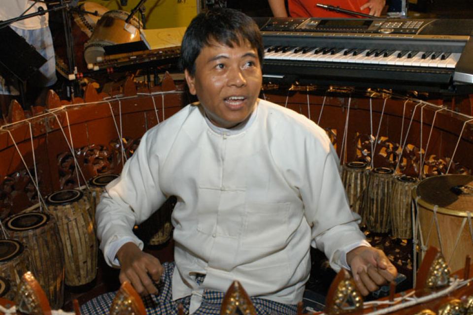 Kyaw Kyaw Naing sits in the center and plays the Burmese circle drum, also known as the pat waing